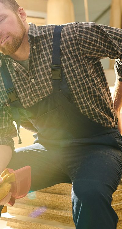 man sitting on wood pile holding back in pain il